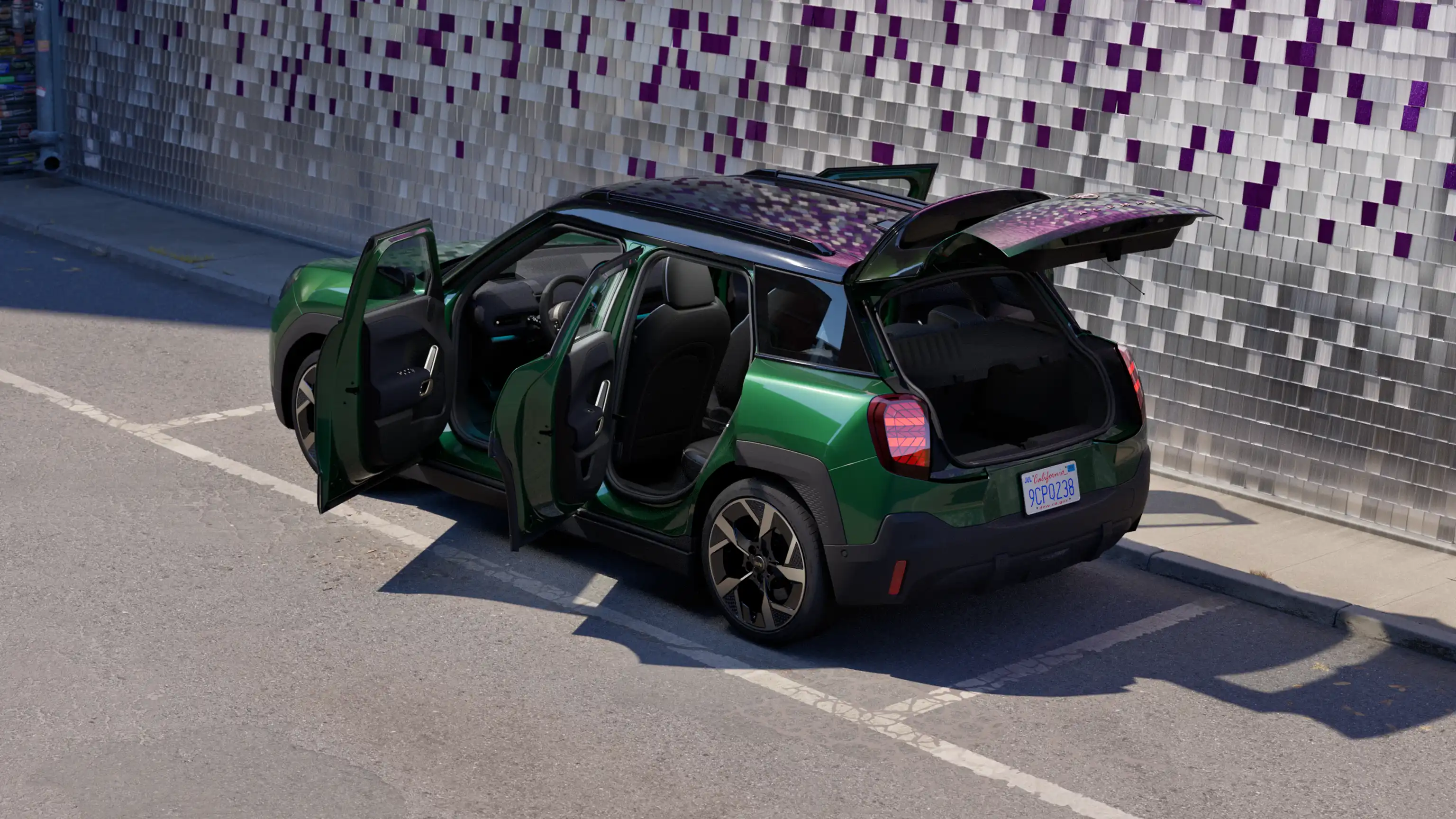 Rear side view of parking all-electric MINI Aceman in British Racing Green in parking lot with all doors open and coloured wall in the background