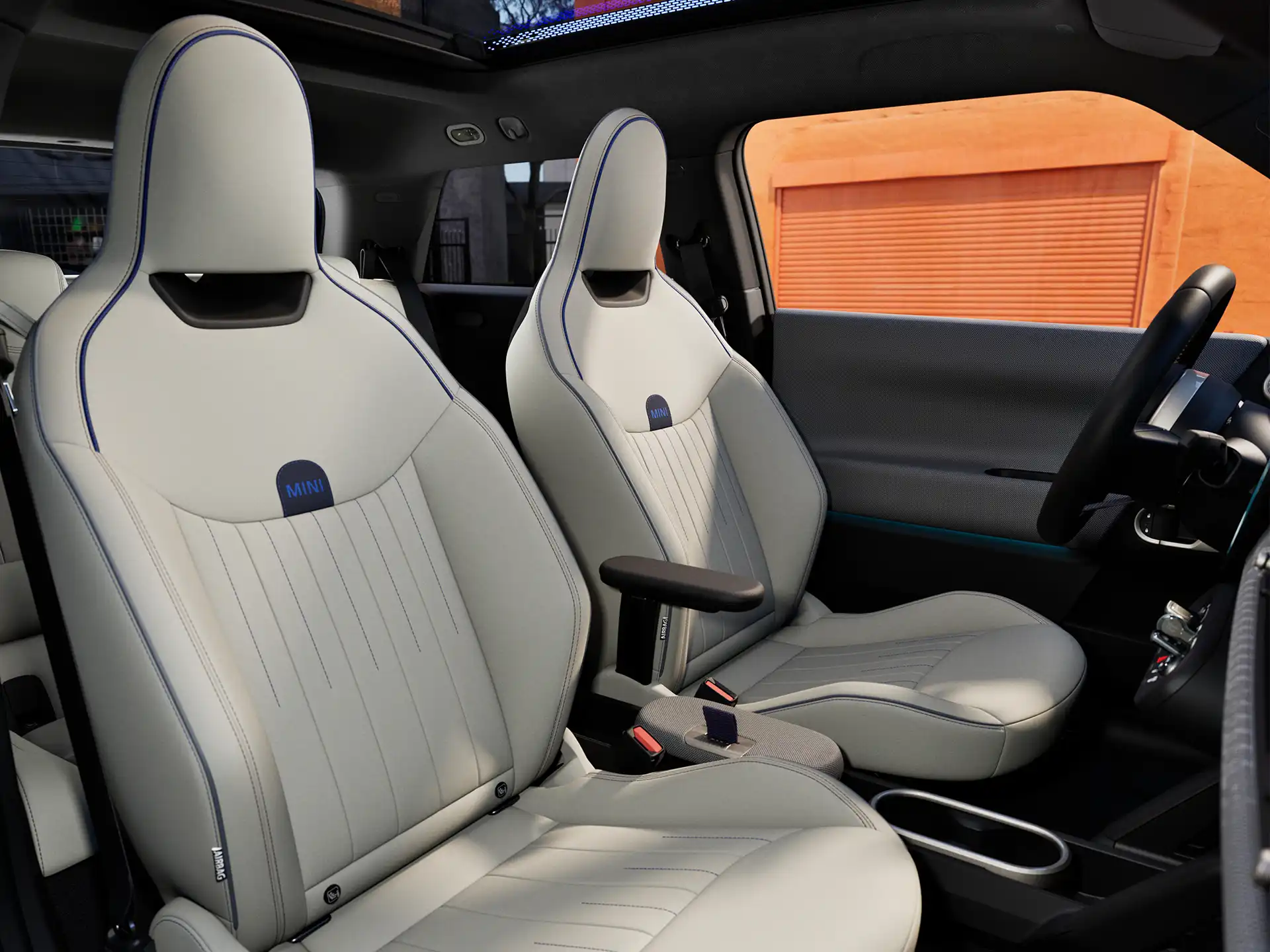 Interior perspective of the all-electric MINI Cooper is showing the dashboard, steering wheel, round display, panorama glassroof and back of the frontseats