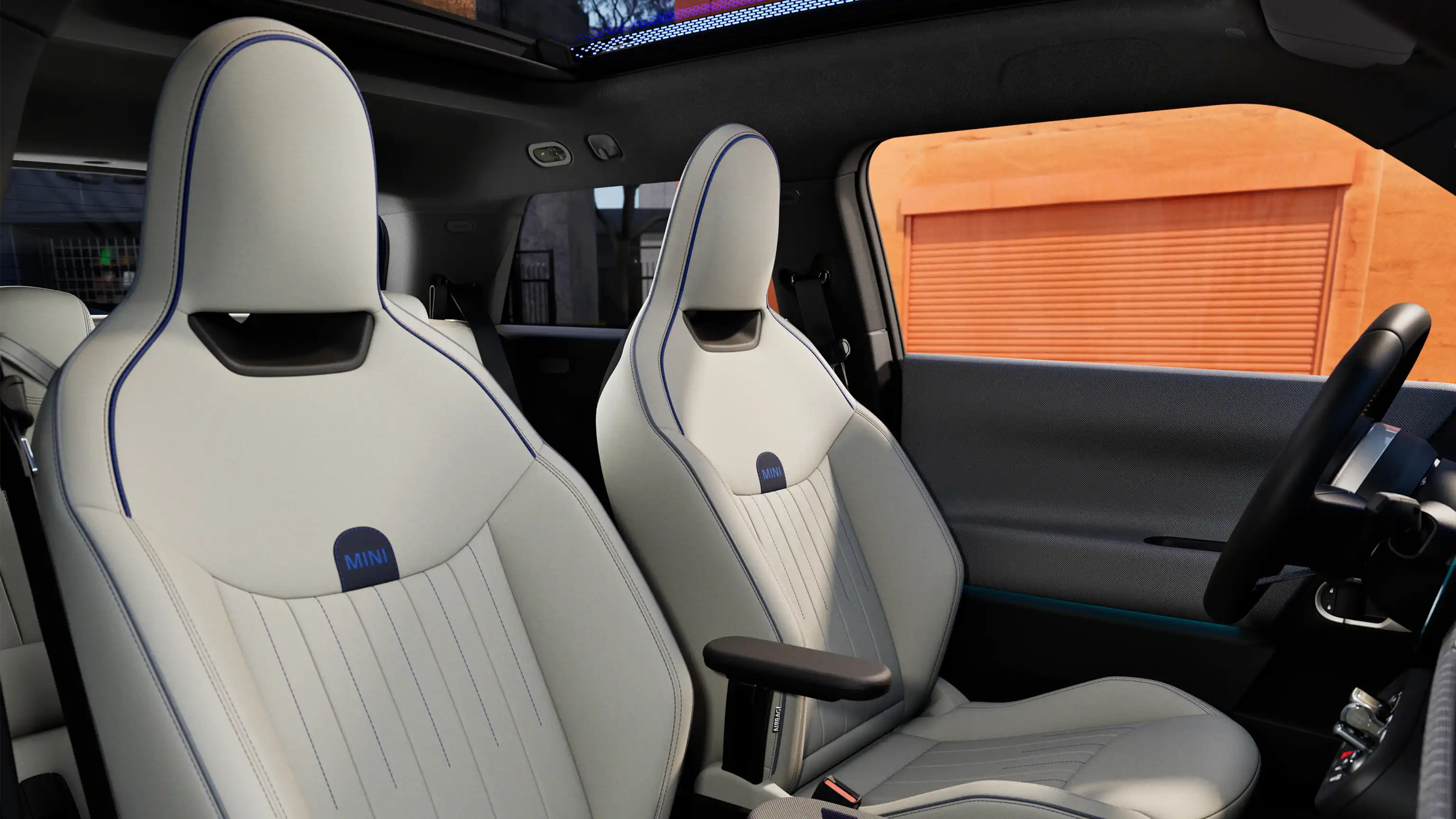 Interior perspective of the all-electric MINI Cooper is showing the dashboard, steering wheel, round display, panorama glassroof and back of the frontseats